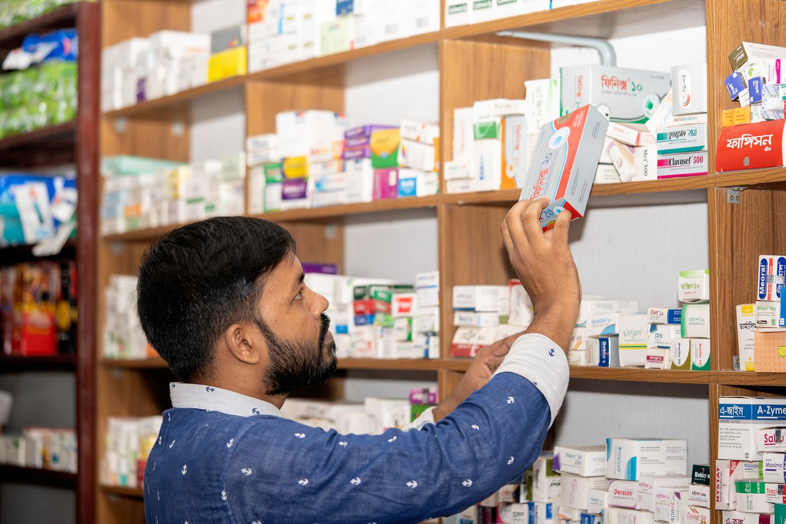 Professionnel vérifiant une boîte de médicaments devant les rayonnages d’une pharmacie.