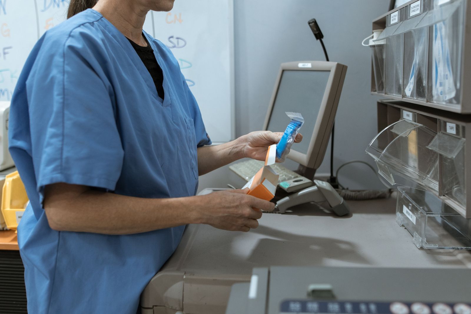 Professionnelle de santé contrôlant un produit conditionné devant des bacs de rangement.